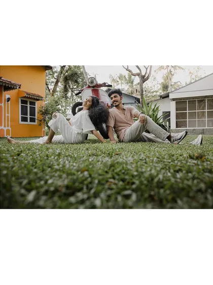 A relaxed and happy shot of a couple sitting on the grass with a scooter.