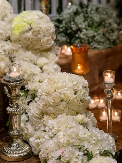 A close-up of a cascading installation of white roses and hydrangeas, with silver candelabras nestled within. The combination of candlelight and dense florals creates a feeling of pure romance.