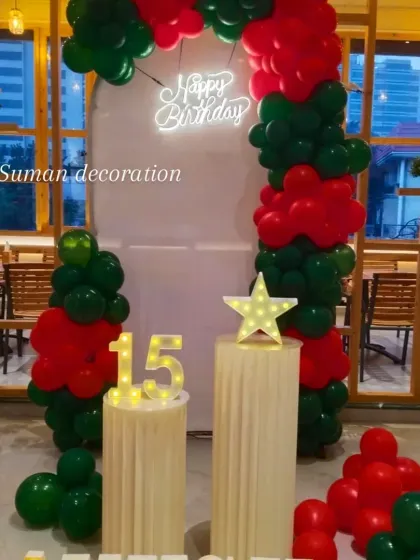 A 15th birthday celebration with a red and green balloon arch. The setup includes a neon sign, a light-up star prop, and the number '15' in marquee lights on plinths.