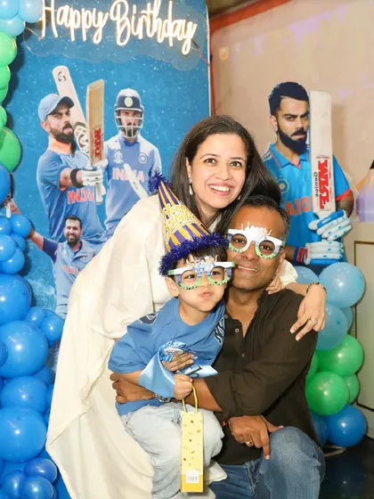 A cricket-themed birthday party for a young sports fan. The family poses with fun props in front of a backdrop featuring famous Indian cricketers.