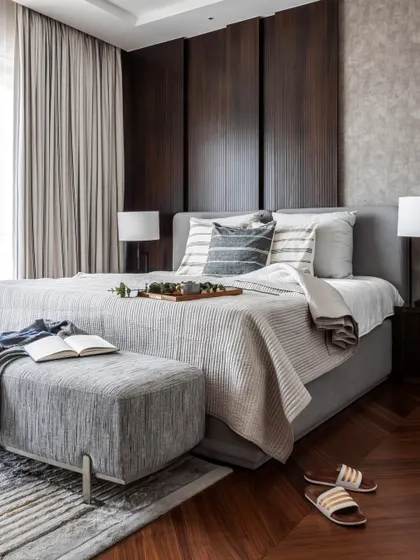 This bedroom is designed for slow mornings and quiet luxury. The warmth of dark wood paneling meets soft, layered grey textiles, creating a space that feels both cozy and contemporary. Herringbone floors add a sense of classic balance to this modern bedroom design.