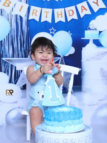 A happy birthday boy plays with his cake topper during his first birthday photoshoot. The cheerful smile and festive blue decorations make this a heartwarming memory.