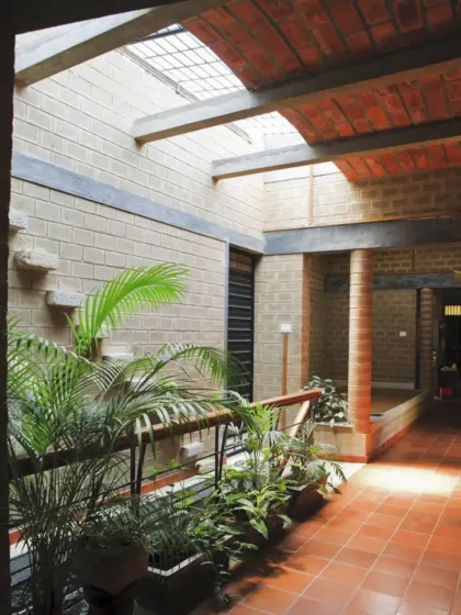 The sunlit corridor of Mr. Petachi's house, featuring exposed brick walls and a skylight. The row of indoor plants adds life and freshness, demonstrating how even transitional spaces can be designed to connect with nature.