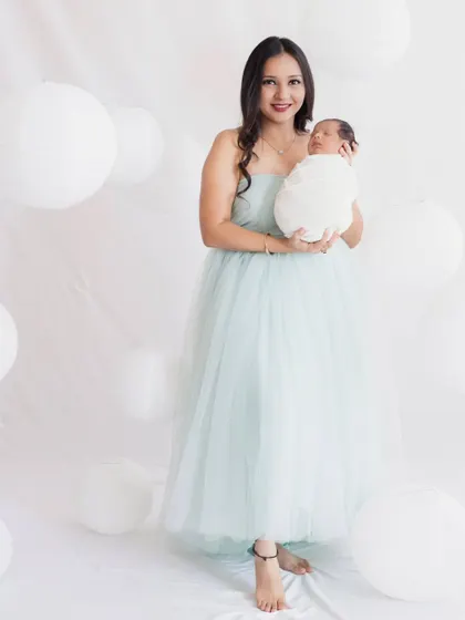 A beautiful full-length portrait of a new mother holding her baby. The ethereal white-on-white theme creates a serene and angelic feel.