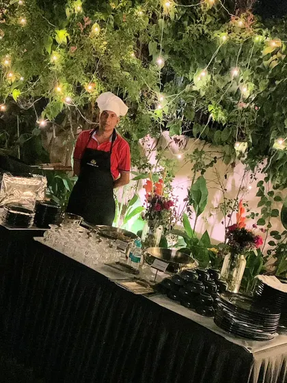 A live tandoori snack counter set against a backdrop of lush greenery and fairy lights for an event at Sainik Farms.