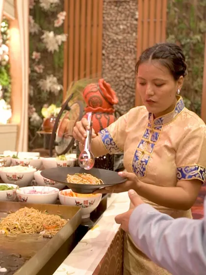 A server at a live noodle station, preparing a custom bowl for a guest. Our team is trained to be attentive and accommodating, ensuring each guest gets exactly what they desire.