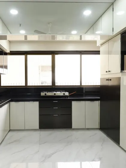 A full view of the black and white kitchen, showing the efficient layout and abundant storage, including overhead cabinets that reach the ceiling. The glossy finish on the cabinets reflects light, making the space feel bright and open.