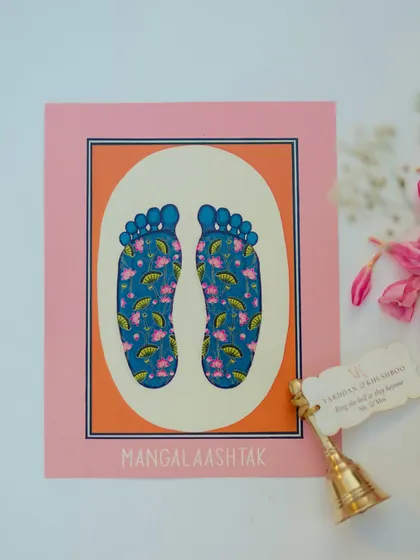 A custom-designed "Mangal Aashtak" card with artistic feet motifs, paired with a small bell, showcasing our attention to personalized and meaningful details.