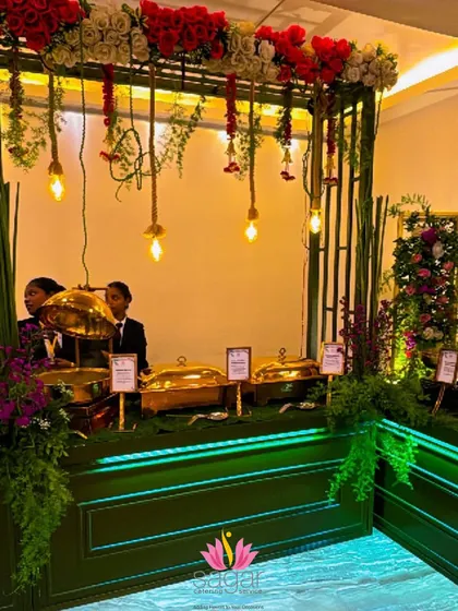 A closer look at the serving area of the Green and Gold buffet. The warm lighting from the hanging bulbs highlights the golden chafing dishes, making the food look even more appetizing.