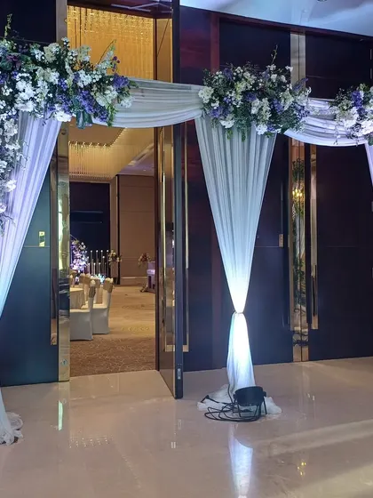 An elegant indoor entrance with white and purple drapes and lush floral toppers.