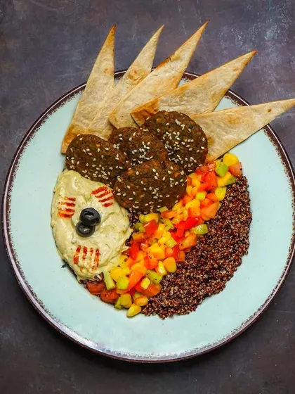 An artistic arrangement of a falafel platter with hummus, quinoa, fresh salsa, and crispy pita chips.
