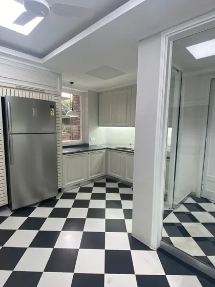 A closer look at the renovated office kitchen, where classic design meets modern functionality. The black and white chequered flooring provides a timeless foundation for the custom white cabinetry and stainless steel appliances.