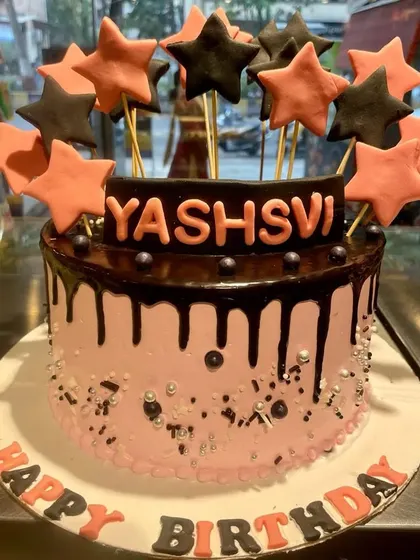 A stylish drip cake with a pink base and dark chocolate ganache. The cake is topped with a burst of black and pink stars for a modern, celebratory look.