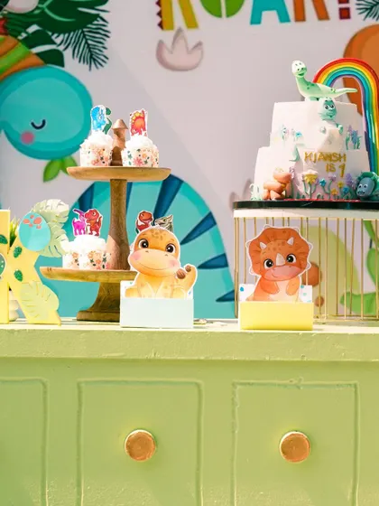 The dessert table with a 'One-O-Saurus' cake and cupcakes. The small dinosaur toppers and props tie the whole theme together.