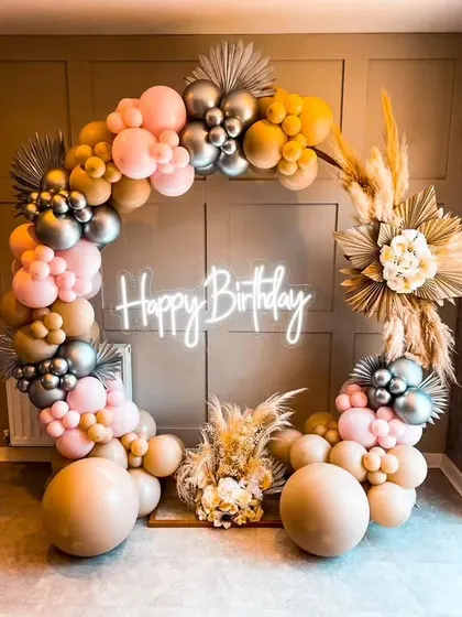 A circular balloon backdrop is a modern and festive choice for a birthday party. This design incorporates a "Happy Birthday" neon sign and is accented with pampas grass for a touch of boho chic.