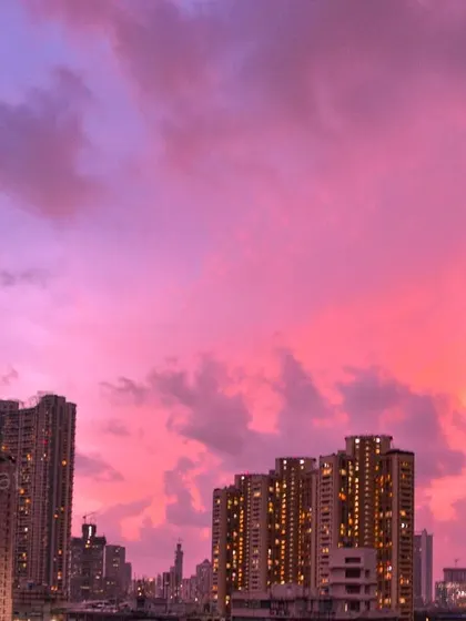 The sky above Mumbai is a brilliant magenta and purple during sunset, with the city's buildings lit up against the colorful display.
