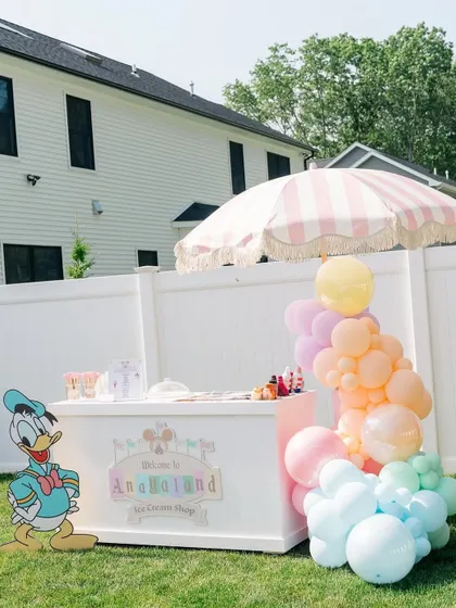 An adorable ice cream cart prop, complete with a striped umbrella and a Donald Duck cutout, adding an interactive and fun element to the party.