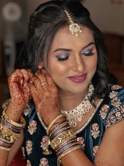 A candid moment of the bride-to-be adjusting her earrings, showing off the intricate details of her bangles and the beautiful eye makeup.