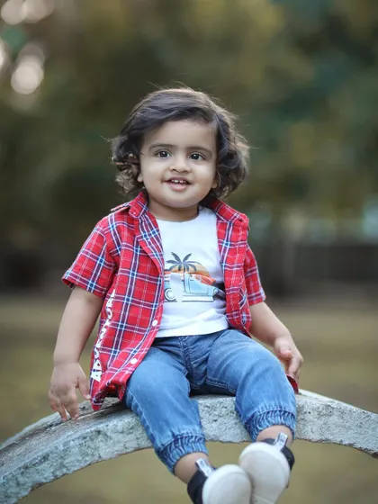 A charming outdoor portrait of a toddler boy with curly hair, sitting on a stone bench. This shot highlights his cute outfit and sweet expression.