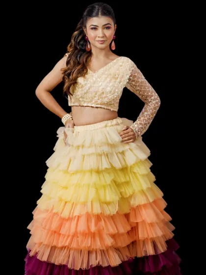 This fun and vibrant tiered lehenga features an ombre effect from yellow to deep magenta. Paired with a sequined one-shoulder blouse, it's a perfect outfit for a sangeet or mehndi party.