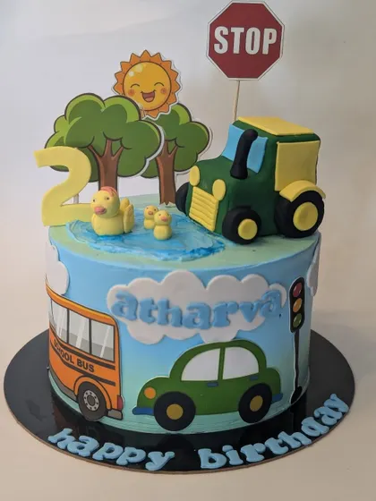 A bright and cheerful "Wheels on the Bus" themed cake. This design includes a school bus, tractor, car, and even little ducks in a pond for a fun second birthday.