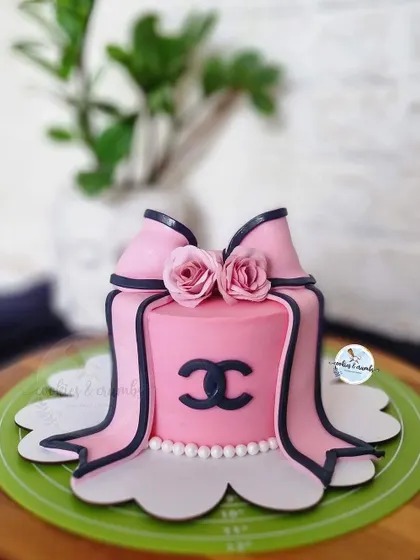 A chic, fashion-inspired cake. This design features a pink buttercream finish, a fondant bow, and the iconic Chanel logo, perfect for a stylish birthday.