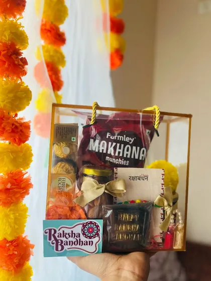 A festive Rakhi gift box held up against a backdrop of marigold flowers, showcasing the traditional theme.
