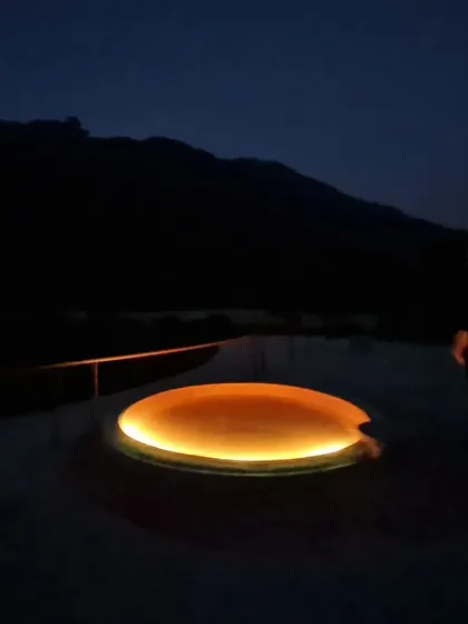 A circular skylight on the terrace glows like a 'Night Sun'. This feature transforms the roof into a celestial map, bringing a touch of warmth and magic to the space after dark and interacting with the mountain's silhouette.
