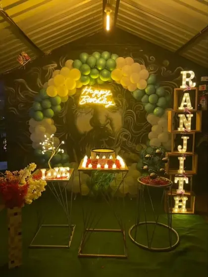 A unique birthday setup in front of a large wall mural, with a green and white balloon arch that complements the artwork.
