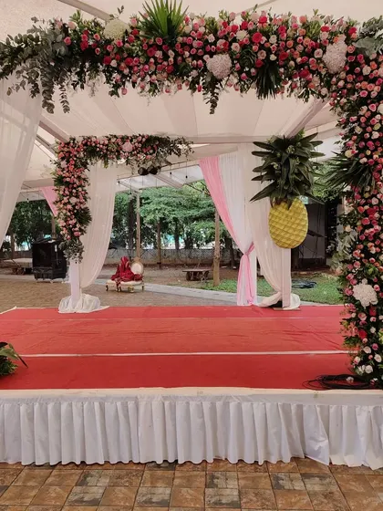 A beautiful outdoor wedding stage with a canopy of pink and white flowers. The unique pineapple-shaped floral arrangements on the pillars add a fun and tropical touch to the decor.