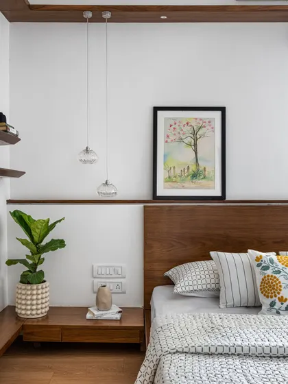A detail of the bedside in the 'Pepper and Coffee' project, showing a floating wooden nightstand, delicate pendant lights, and a beautiful watercolor painting, adding a personal and artistic touch.