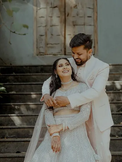 A couple shares a sweet, smiling moment on a staircase, surrounded by greenery. This image captures the relaxed and happy atmosphere of their celebration.