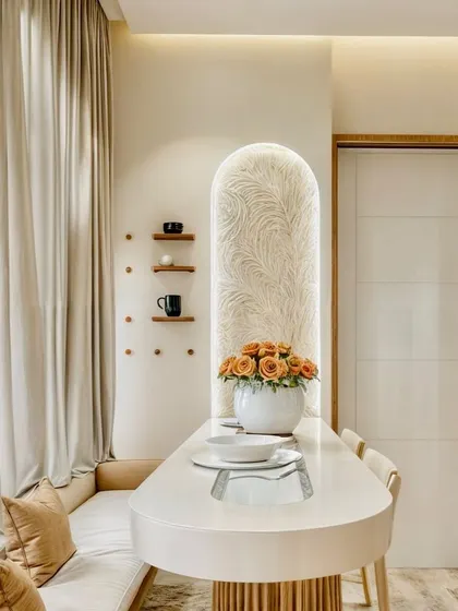 This dining area is a perfect example of Japandi design, which blends Japanese minimalism with Scandinavian functionality. The space is defined by a textured arched niche, a sleek dining table with a fluted base, and soft, neutral tones. The result is a dining nook that feels both cozy and clutter-free.