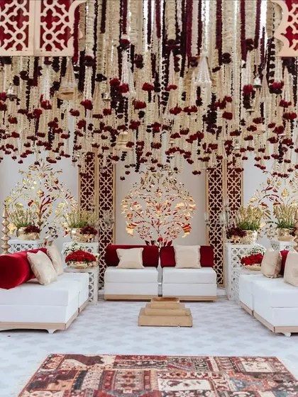 The main stage area for the 'Laal Ishq' wedding, featuring a breathtaking ceiling of hanging rajnigandha and rose garlands. The white seating with red accents provides a beautiful contrast to the rich floral decor.