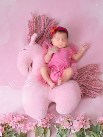 Sparkles, smiles, and unicorn dreams. This sweet baby girl is resting on a large, soft unicorn plush against a magical pink backdrop.