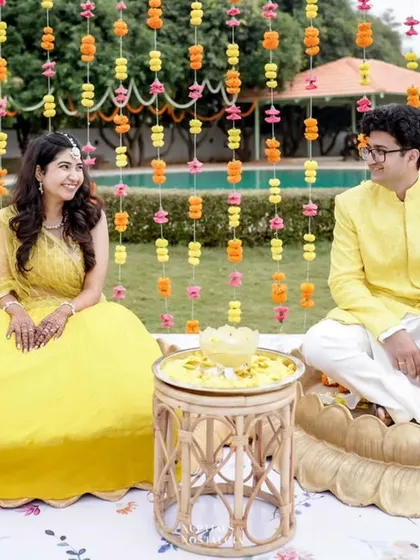 A candid moment during a Haldi ceremony, set against a backdrop of hanging marigold and carnation garlands.
