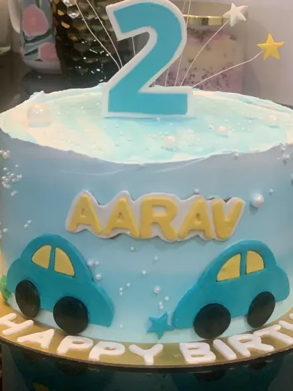 A simple blue car cake for a second birthday. The cake is personalized with the birthday boy's name and decorated with two little cars.