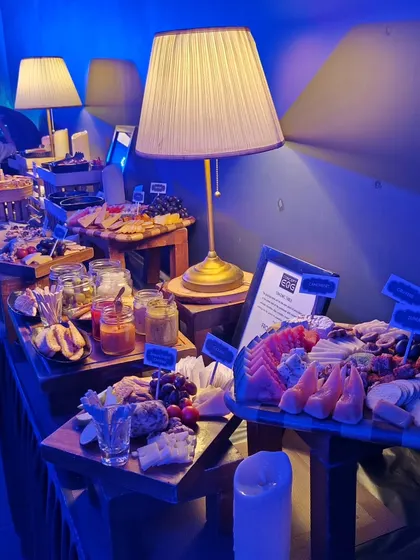 A wide view of the sustainable, farm-to-plate grazing table at the Mercedes-EQ launch. The moody blue lighting of the event highlights the rustic wooden crates and elegant food presentation.