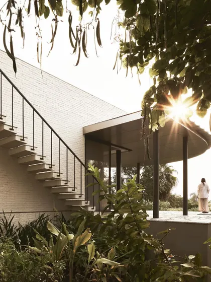 The sun shines through the trees onto the terrace of Pavilion House, highlighting the elegant staircase and curved roofline.