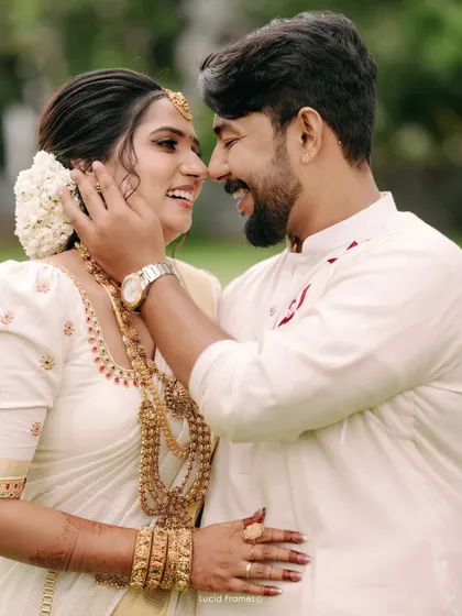 The beautiful smiles of a newly married couple, captured in a close-up that highlights the bride's traditional Kerala jewelry and the groom's loving touch.