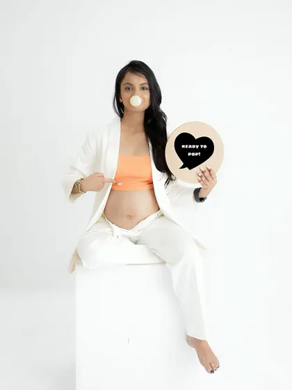 A fun and playful announcement photo. The mom-to-be points to her bump with a "Ready to Pop" sign, a bubble of gum adding to the whimsy.