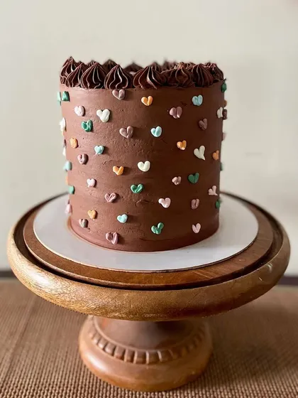 A tall chocolate cake that's as cute as it is delicious. The rich chocolate buttercream is covered in tiny, multi-colored piped hearts, making it a sweet and simple design for any birthday.