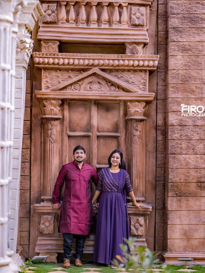 A couple stands before a grand, stone-carved doorway, a backdrop that adds a sense of history and importance to the photograph.