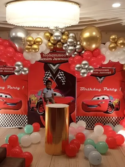 A Disney Cars themed birthday party. The backdrop features Lightning McQueen, and the balloon arch uses the signature red, silver, and gold colors.