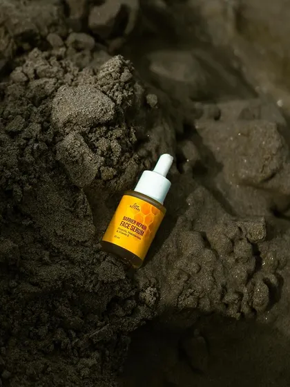 Shine bright no matter the light. An outdoor shot of a face serum bottle nestled in wet sand, using natural elements to create a raw and earthy feel for this skincare product.