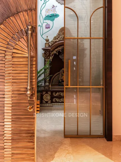 The entrance to the sacred space is just as important as the space itself. Here, a beautifully crafted wooden door with a fan-like pattern and a sleek glass door with brass trim lead into the mandir.