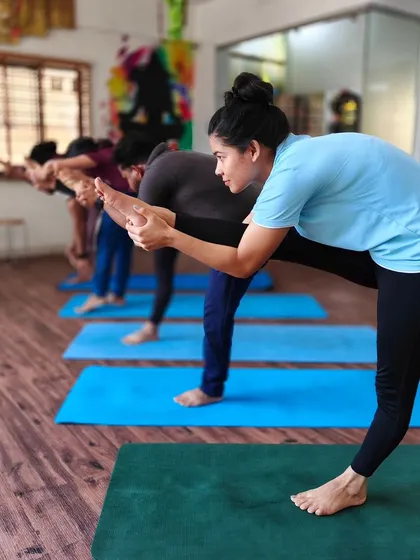 Students practice a standing forward bend variation, focusing on hamstring flexibility and balance.