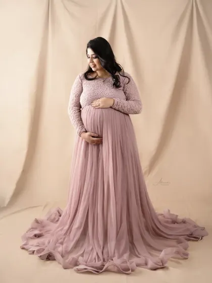 A quiet, contemplative moment. The mom-to-be looks down at her bump, captured in our studio with a soft, neutral background and a beautiful pink lace gown.