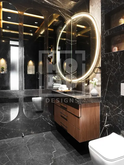 A large, backlit oval mirror brings a soft glow to this moody black marble bathroom. It provides excellent task lighting while enhancing the room's luxurious atmosphere.