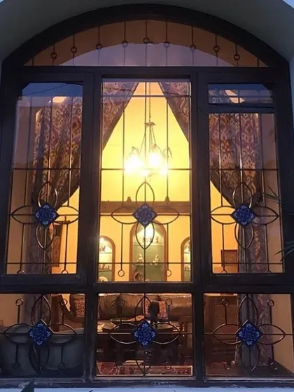 Seen from the outside at night, the large arched window of the Roopa Hariprasad Residence glows like a lantern. The intricate pattern of the custom grille is silhouetted against the warm interior light, creating a dramatic architectural feature.